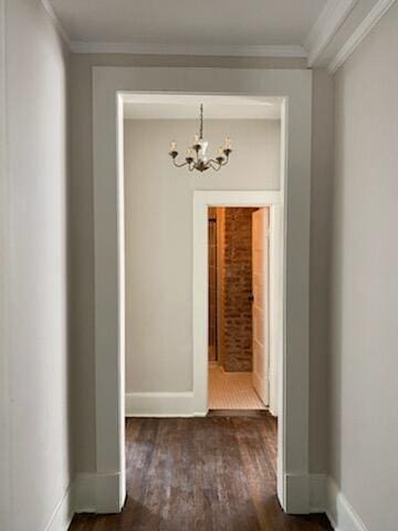 hallway featuring dark wood-type flooring, ornamental molding, and a chandelier