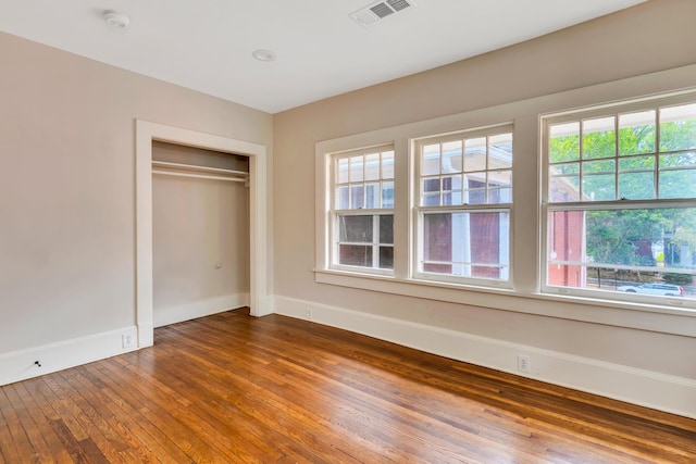 unfurnished bedroom with a closet, wood-type flooring, and multiple windows