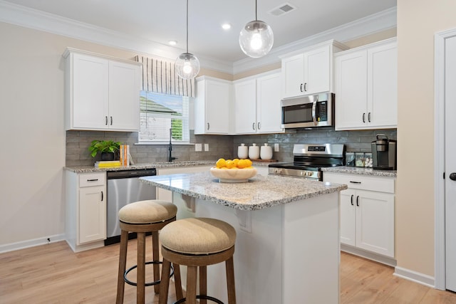 kitchen featuring decorative light fixtures, stainless steel appliances, white cabinetry, and a kitchen island