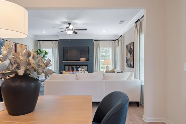 living room featuring ceiling fan, light hardwood / wood-style floors, ornamental molding, and a fireplace