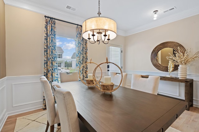 dining area featuring a healthy amount of sunlight, light wood-type flooring, ornamental molding, and an inviting chandelier