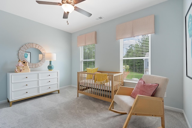 bedroom with ceiling fan, light carpet, and a nursery area