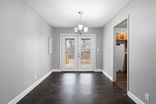 unfurnished dining area featuring crown molding, french doors, dark hardwood / wood-style floors, and an inviting chandelier