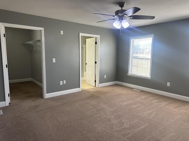 unfurnished bedroom with a spacious closet, light colored carpet, ceiling fan, a textured ceiling, and a closet