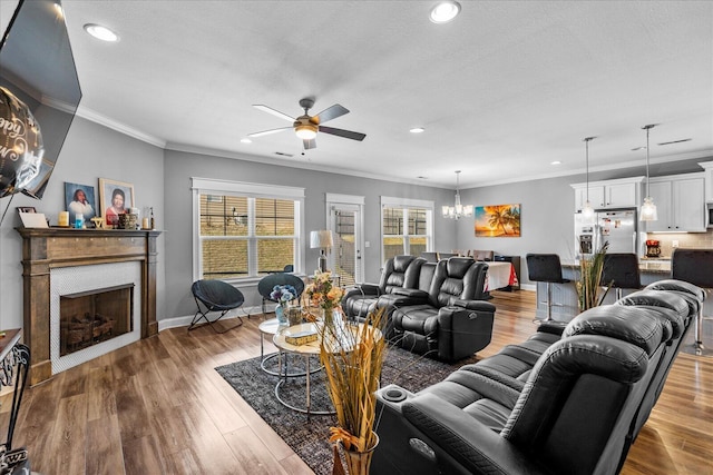 living room with a textured ceiling, hardwood / wood-style flooring, ceiling fan with notable chandelier, and ornamental molding