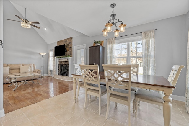 tiled dining space with ceiling fan with notable chandelier, a fireplace, and vaulted ceiling