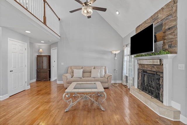 living room featuring hardwood / wood-style floors, high vaulted ceiling, ceiling fan, and a stone fireplace