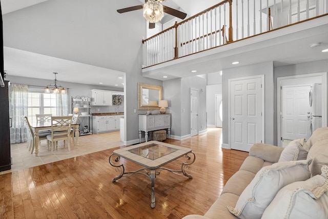 living room featuring light hardwood / wood-style flooring, ceiling fan with notable chandelier, and a high ceiling