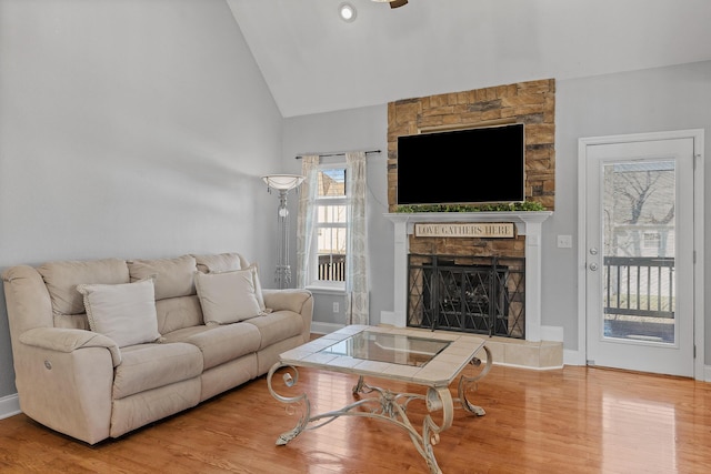 living room with hardwood / wood-style flooring, a stone fireplace, and high vaulted ceiling