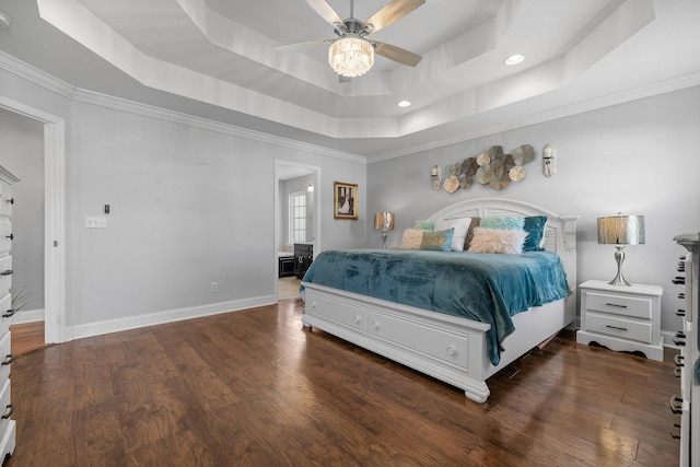 bedroom with crown molding, ceiling fan, connected bathroom, a tray ceiling, and dark hardwood / wood-style flooring