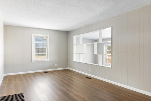 empty room with plenty of natural light, dark hardwood / wood-style floors, and a textured ceiling