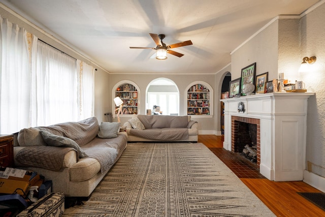 living room featuring built in shelves, ceiling fan, a brick fireplace, dark hardwood / wood-style floors, and ornamental molding