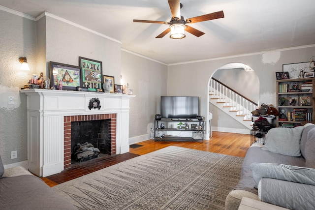 living room with a fireplace, wood-type flooring, ceiling fan, and ornamental molding