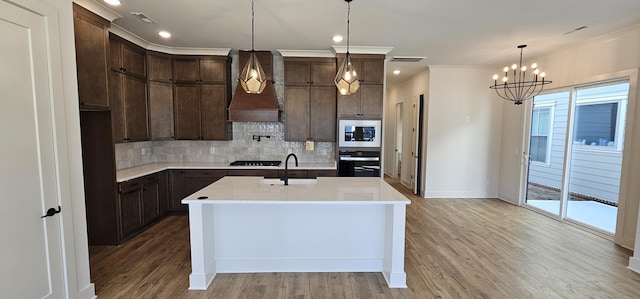 kitchen featuring sink, a kitchen island with sink, black appliances, custom range hood, and decorative backsplash