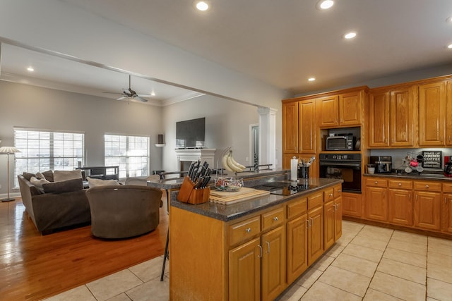 kitchen featuring light tile patterned floors, a breakfast bar area, a kitchen island, black appliances, and ornamental molding