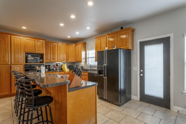 kitchen with a breakfast bar, black appliances, light tile patterned floors, a center island with sink, and dark stone countertops