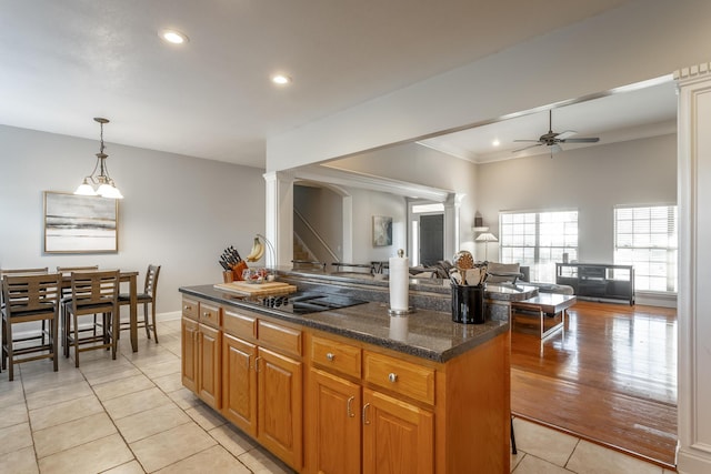 kitchen featuring ceiling fan, a kitchen island, dark stone countertops, decorative light fixtures, and light tile patterned floors