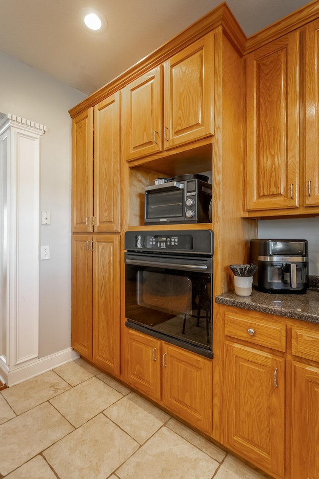 kitchen featuring light tile patterned floors, black oven, and dark stone counters