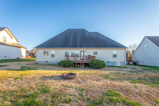 back of house featuring a fire pit, a deck, and a lawn