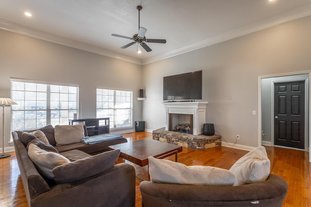 living room featuring light hardwood / wood-style floors, a stone fireplace, ceiling fan, and ornamental molding