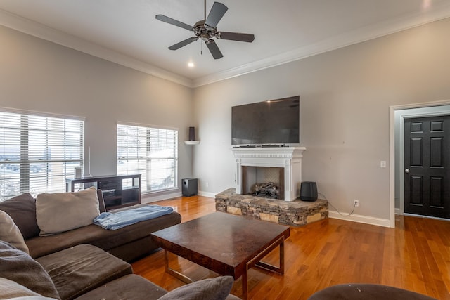 living room with light wood-type flooring, a stone fireplace, ceiling fan, and ornamental molding