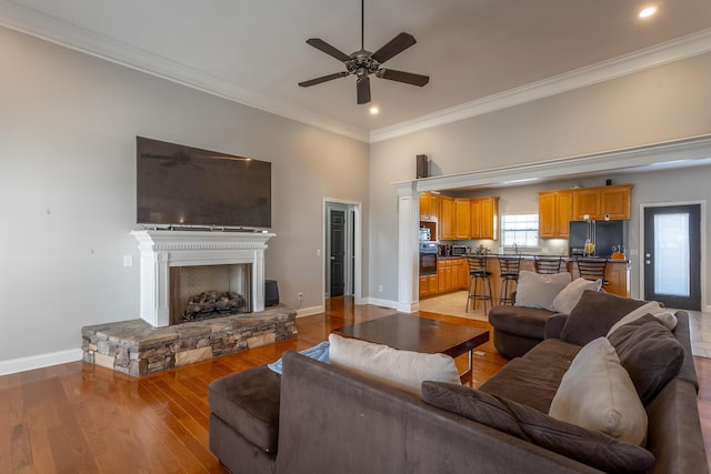 living room with ceiling fan, light wood-type flooring, a fireplace, and ornamental molding