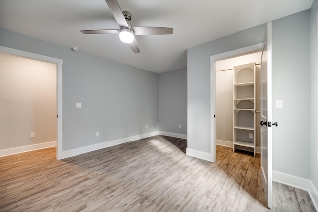 unfurnished bedroom with ceiling fan, a closet, a spacious closet, and light hardwood / wood-style flooring