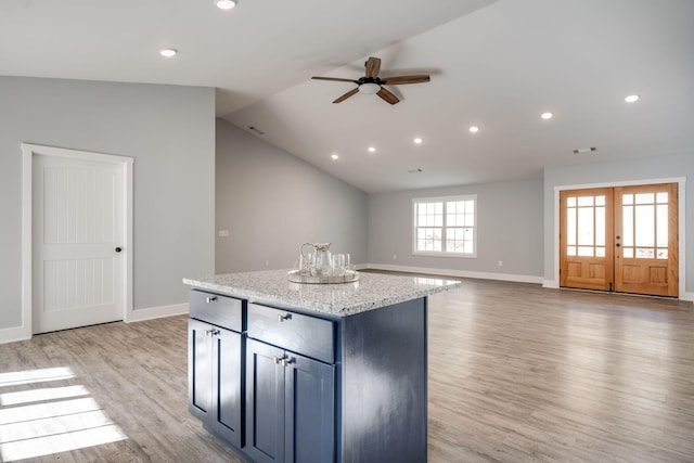 kitchen with light stone countertops, vaulted ceiling, ceiling fan, a center island, and light hardwood / wood-style floors