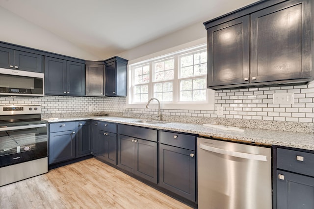 kitchen with light stone countertops, appliances with stainless steel finishes, vaulted ceiling, sink, and light hardwood / wood-style flooring