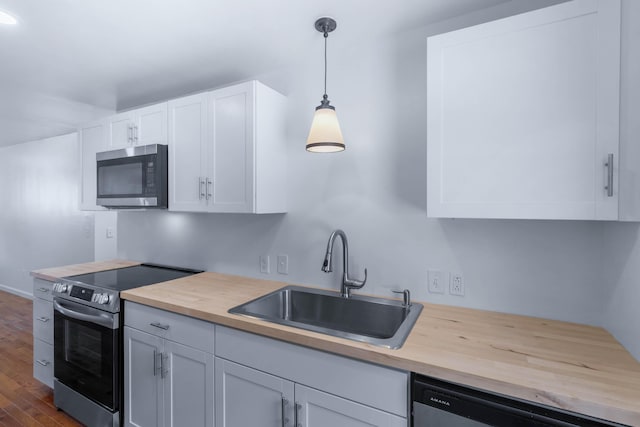 kitchen with sink, dark hardwood / wood-style floors, appliances with stainless steel finishes, decorative light fixtures, and white cabinetry