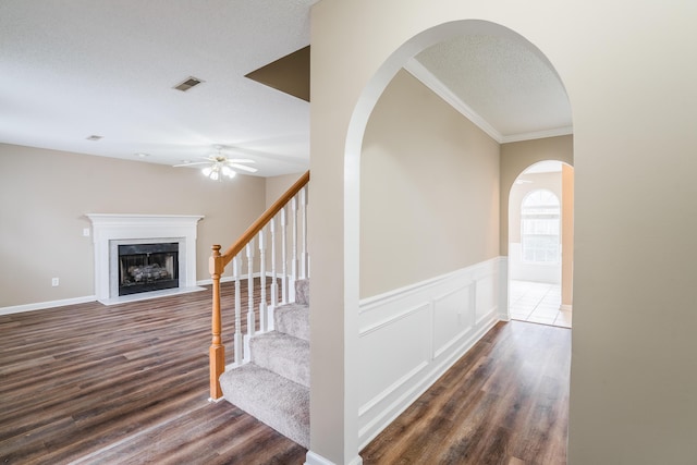 staircase with a textured ceiling, hardwood / wood-style flooring, ceiling fan, and ornamental molding