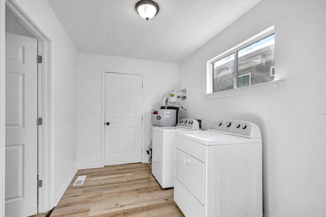 laundry area featuring water heater, light wood-type flooring, and washing machine and clothes dryer