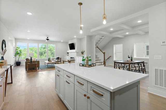 kitchen with beam ceiling, ceiling fan, pendant lighting, light hardwood / wood-style floors, and a kitchen island