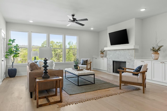 living room featuring ceiling fan, light wood-type flooring, and a tiled fireplace