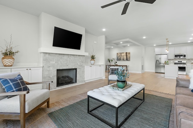 living room featuring light wood-type flooring, ceiling fan, and a tiled fireplace