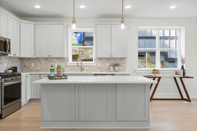 kitchen with white cabinetry, sink, decorative light fixtures, a kitchen island, and appliances with stainless steel finishes