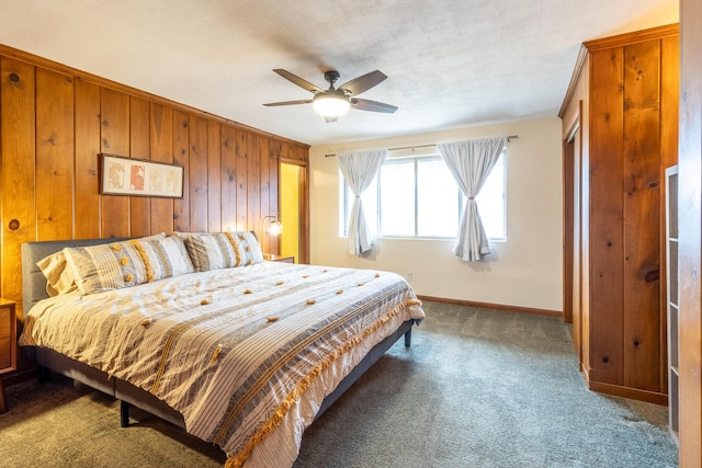 bedroom featuring wooden walls, ceiling fan, and dark colored carpet