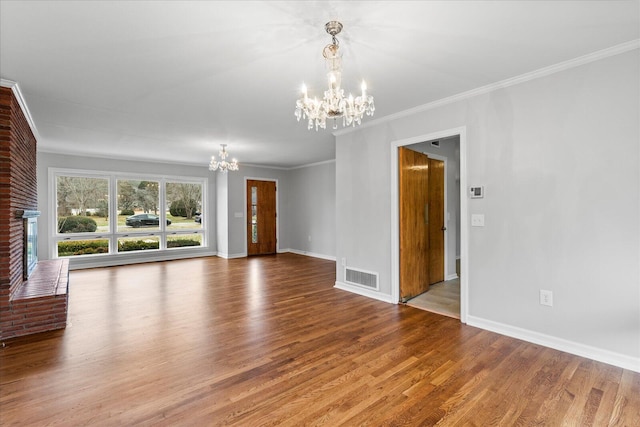 unfurnished living room featuring an inviting chandelier, crown molding, a fireplace, and hardwood / wood-style flooring