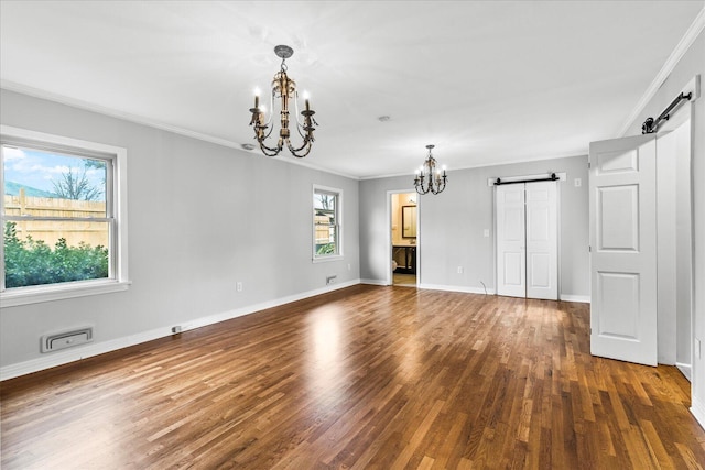 empty room with ornamental molding, a chandelier, a barn door, and dark wood-type flooring