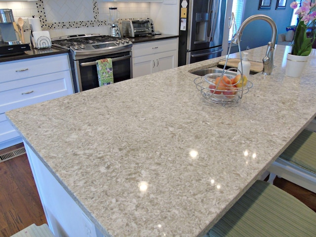 kitchen featuring white cabinetry, light stone countertops, decorative backsplash, and stainless steel appliances