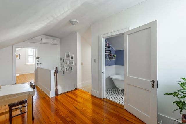 corridor with a wall unit AC, lofted ceiling, and wood-type flooring