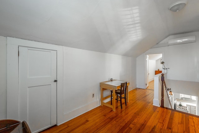 additional living space featuring wood-type flooring, a wall unit AC, and vaulted ceiling