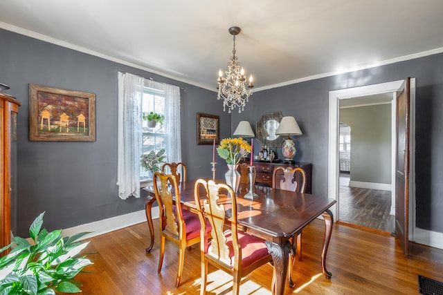 dining space with wood-type flooring, crown molding, and a chandelier