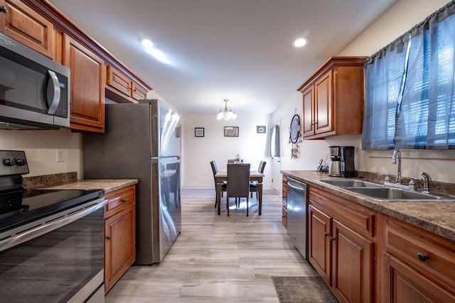 kitchen with appliances with stainless steel finishes, sink, pendant lighting, a notable chandelier, and light hardwood / wood-style floors