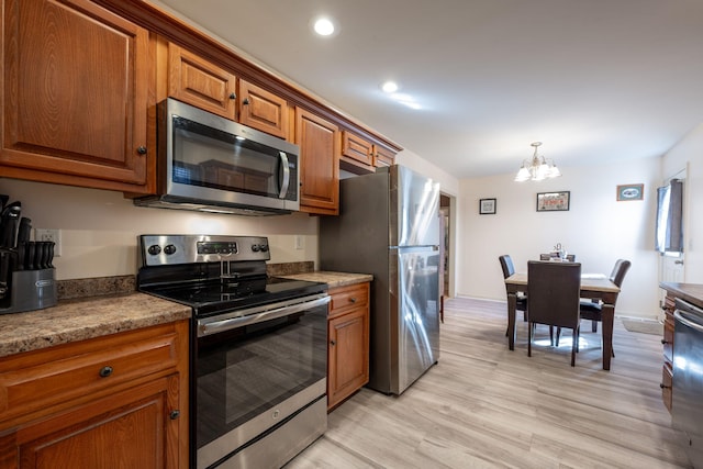 kitchen featuring light hardwood / wood-style flooring, light stone counters, stainless steel appliances, and an inviting chandelier