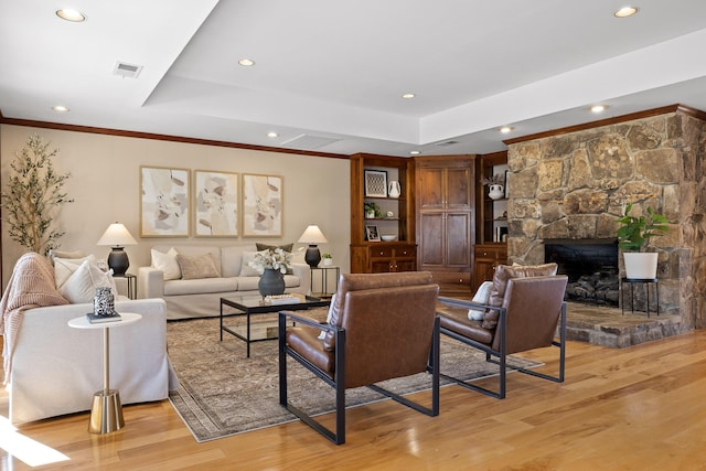 living room with a tray ceiling, a stone fireplace, and light hardwood / wood-style flooring