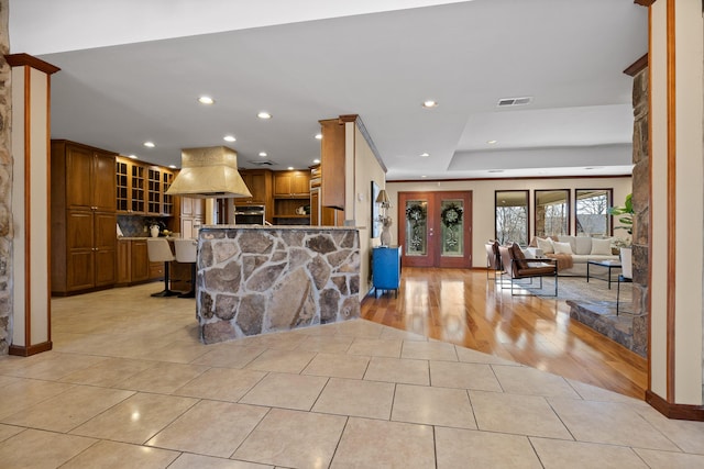 interior space featuring light tile patterned floors, a breakfast bar, range hood, kitchen peninsula, and oven