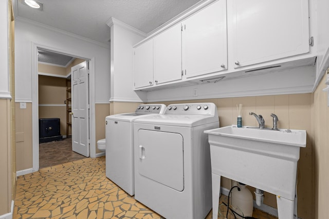 clothes washing area featuring sink, cabinets, washing machine and clothes dryer, crown molding, and a textured ceiling