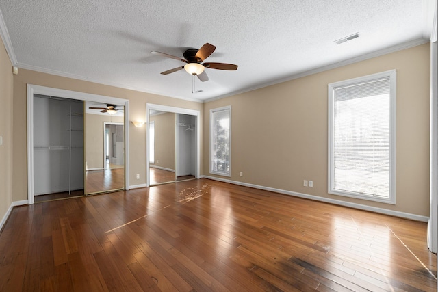 unfurnished bedroom with multiple windows, dark wood-type flooring, and multiple closets