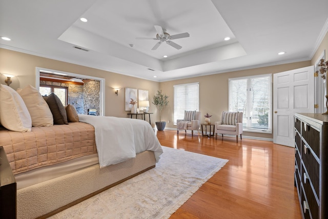 bedroom with crown molding, light hardwood / wood-style floors, a raised ceiling, and ceiling fan